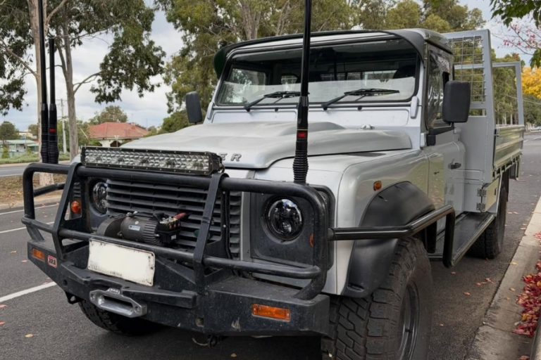 Land Rover Defender 130 tray ute with ARB bull bar, twin antennas and light bar — tradie fitout for a Strathdale customer.