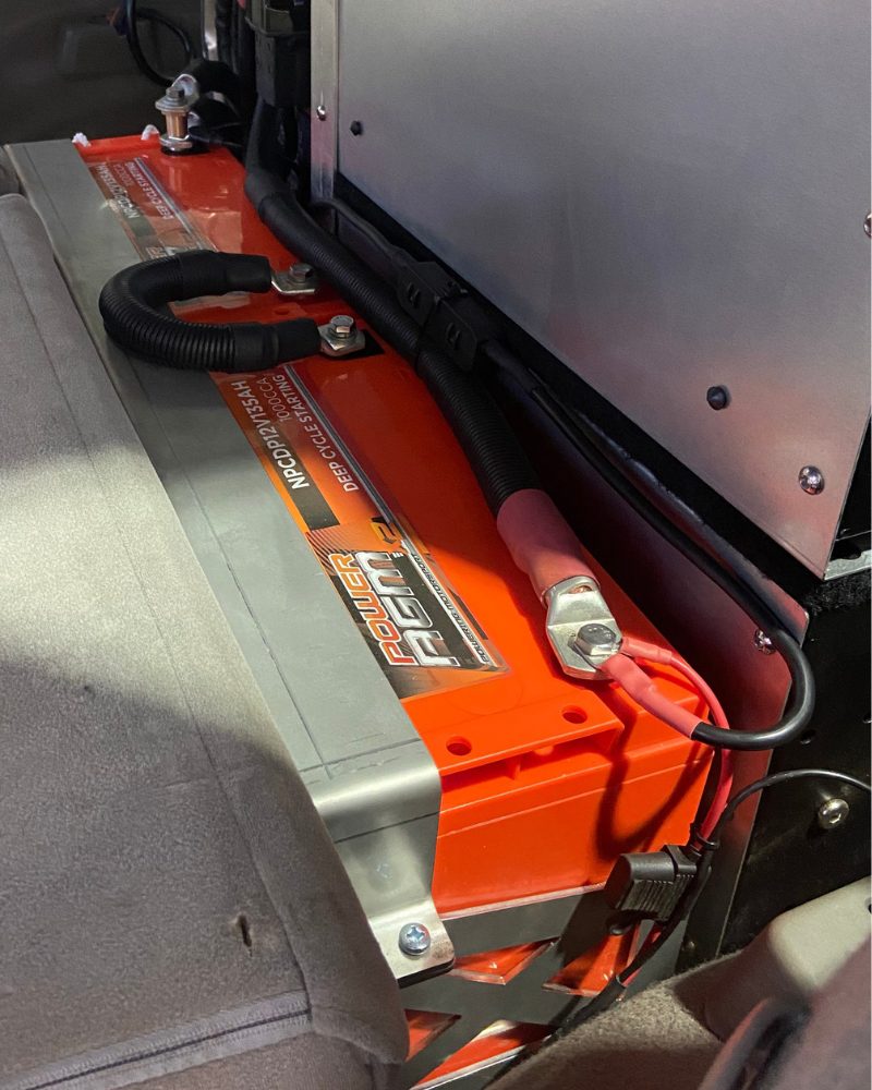 Left side of a custom laser-cut cradle holding twin 135Ah AGM batteries wired in series for 24-volt winch output behind the rear seats of a Nissan GU Patrol, fitted by MBC 4X4 Solutions in Eaglehawk